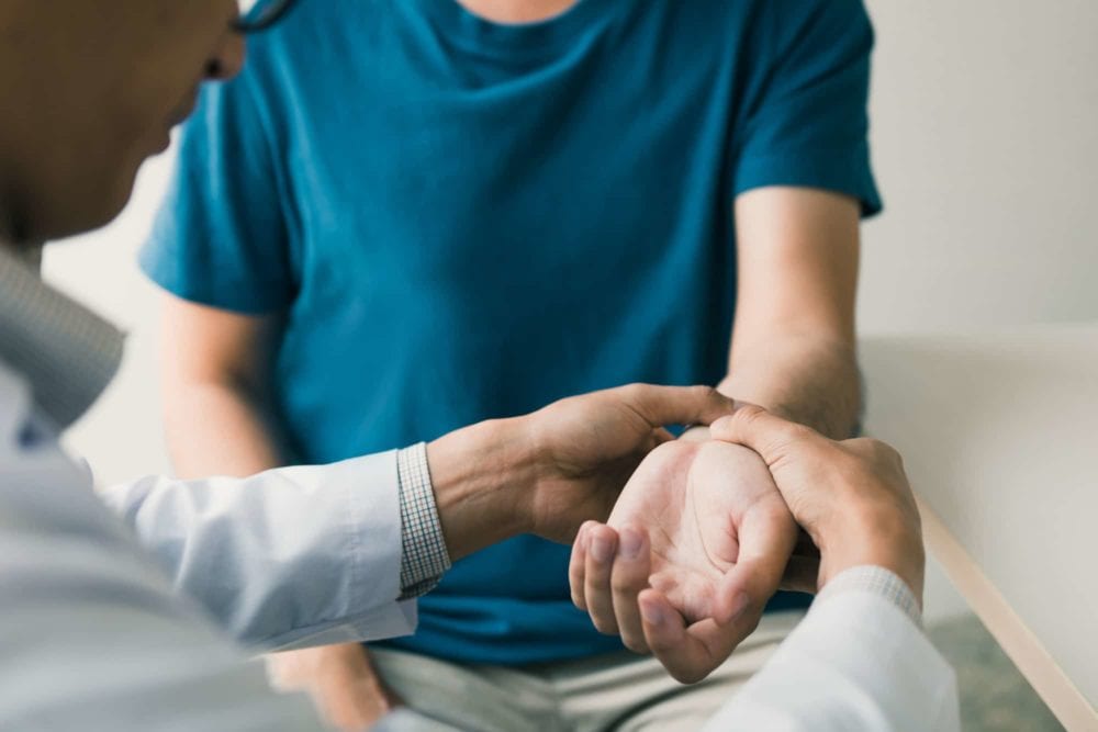 Physical therapist checks the patient wrist by pressing the wrist bone in clinic room e1620668839334
