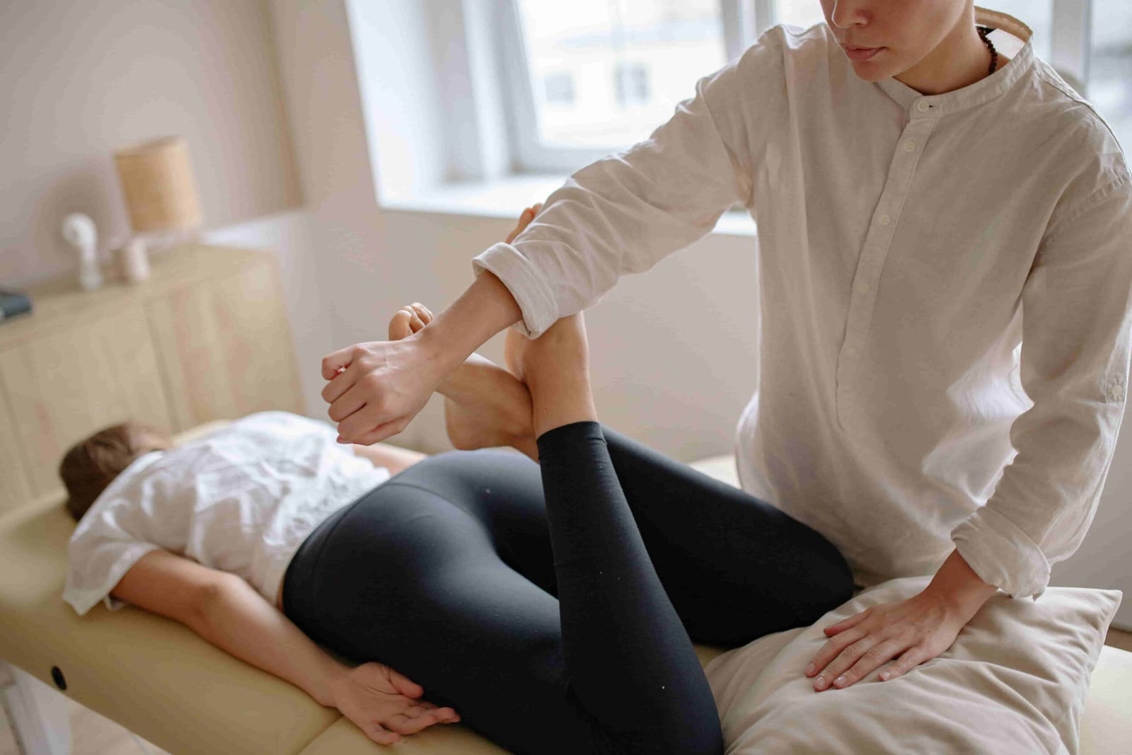 A person lies on a massage table while another person in a white shirt stretches their leg, possibly providing relief for sciatica in a therapy or rehabilitation setting.