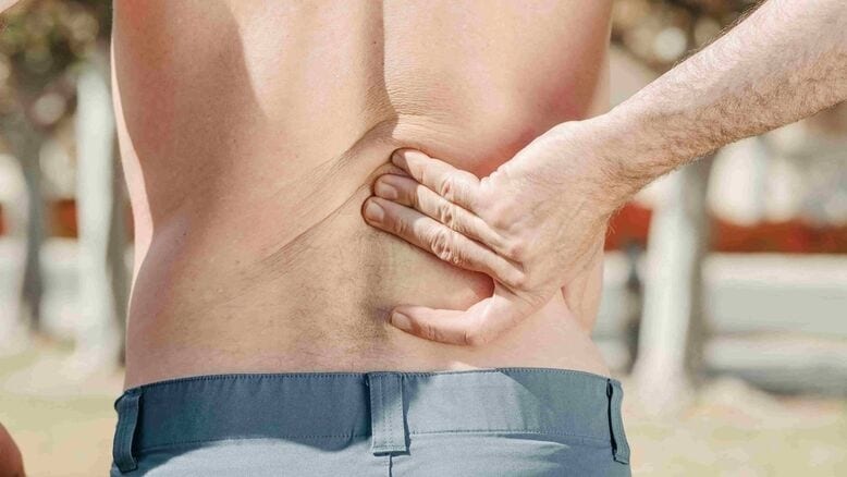 A person wearing blue pants holds their lower back with one hand, suggesting possible back pain or discomfort, this may indicate a need for physiotherapy treatments.