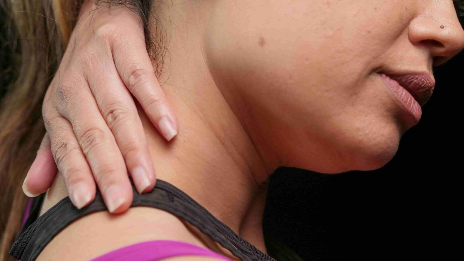 A woman touching the side of her neck with her hand, appearing to apply pressure or massage the area, raising the question: Should I Visit a Physiotherapist or a Massage Therapist for Muscle Pain?.