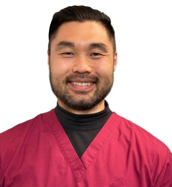 Smiling Asian man wearing a maroon scrub top and a black turtleneck, posing against a white background.