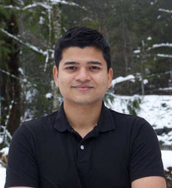 A man in a black shirt smiling at the camera with a snowy forest background, part of his team's outdoor retreat.
