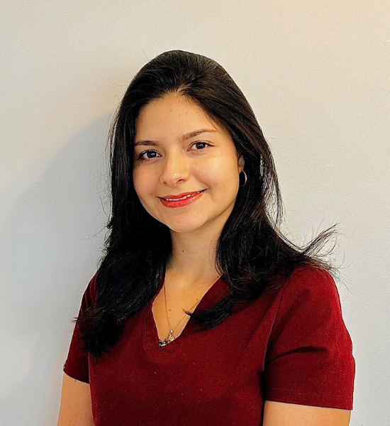 A woman with long black hair, wearing a red top and a subtle smile, stands against a plain background, embodying the warmth and professionalism of Our Team.