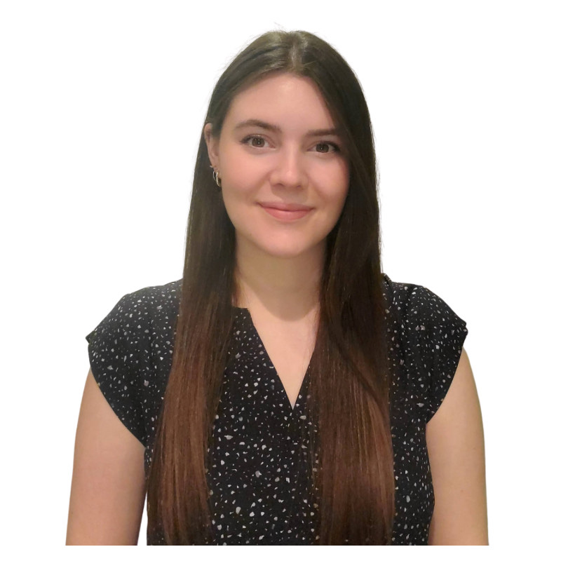 A woman with long brown hair and a black short-sleeved top with white spots stands against a plain white background, representing the core values of her company's collaborative spirit.