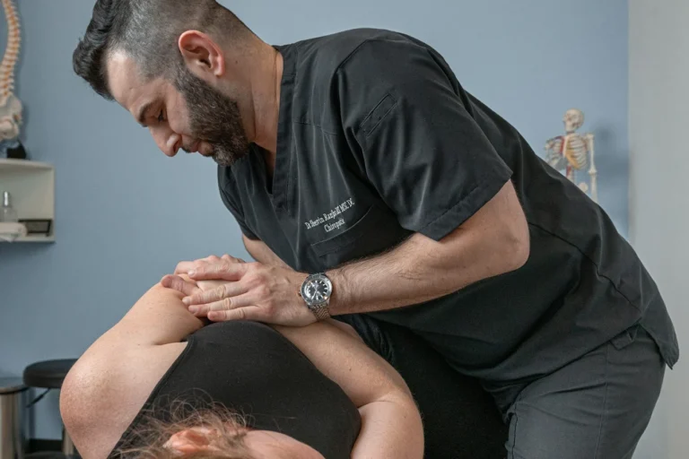 A chiropractor performs an adjustment on a patient's shoulder in a clinical setting.