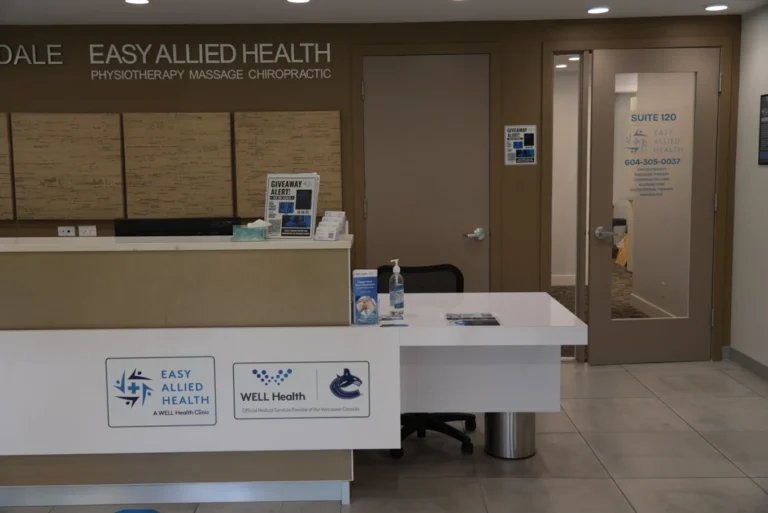 Reception area of Easy Allied Health clinic, featuring a front desk with sanitizer, brochures, and signage for physiotherapy, massage, and chiropractic services. A door labeled Suite 120 is visible.