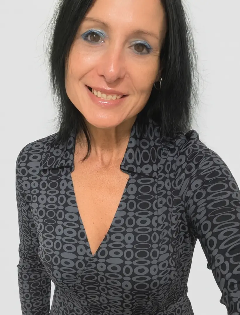 Woman with straight black hair wearing a patterned, long-sleeve dress with a V-neckline, smiling at the camera against a plain white background.