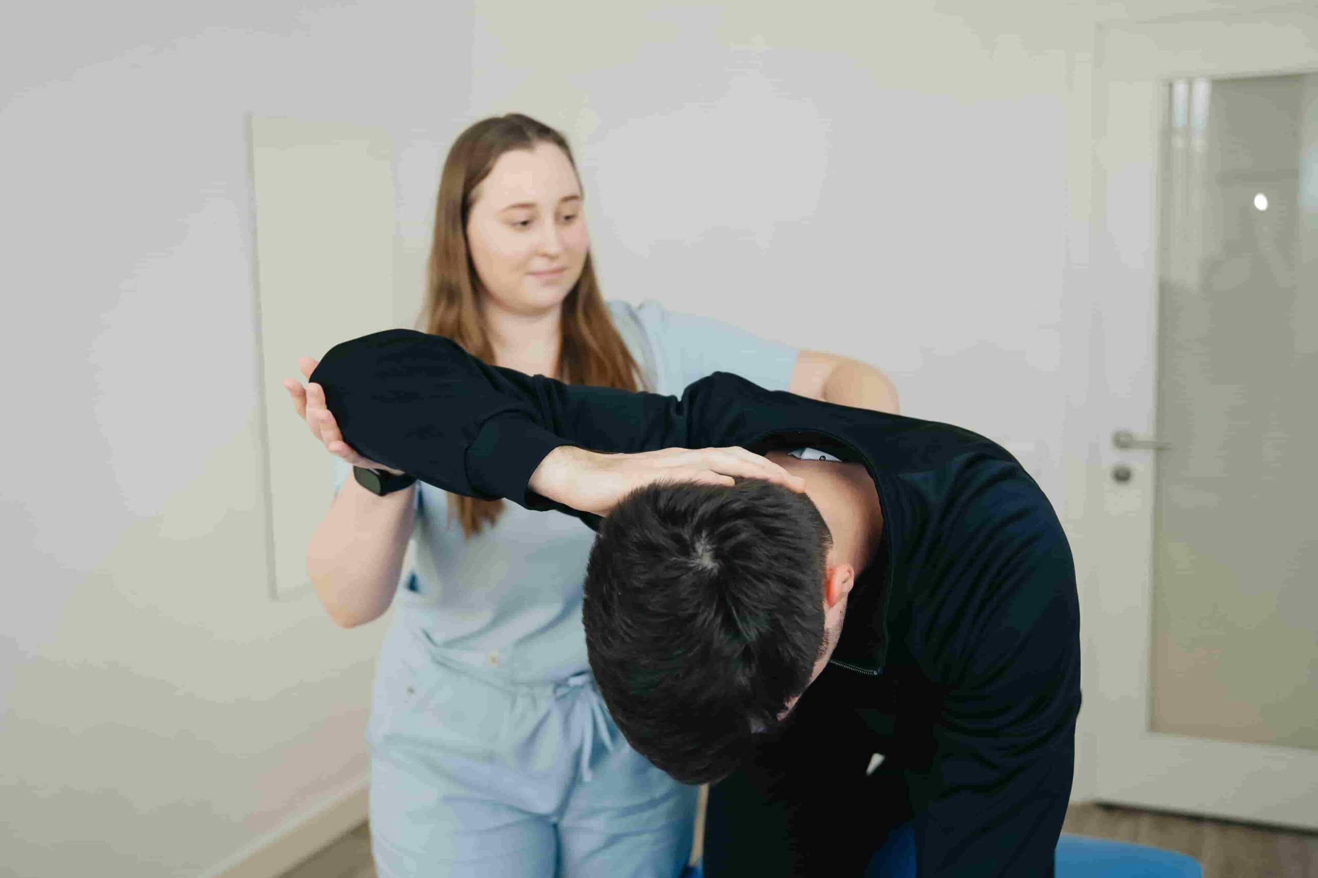 A physical therapist helps a person stretch their upper body during a rehabilitation session in a clinic, answering the question: Can physiotherapy help with workplace injury recovery in Coquitlam?.