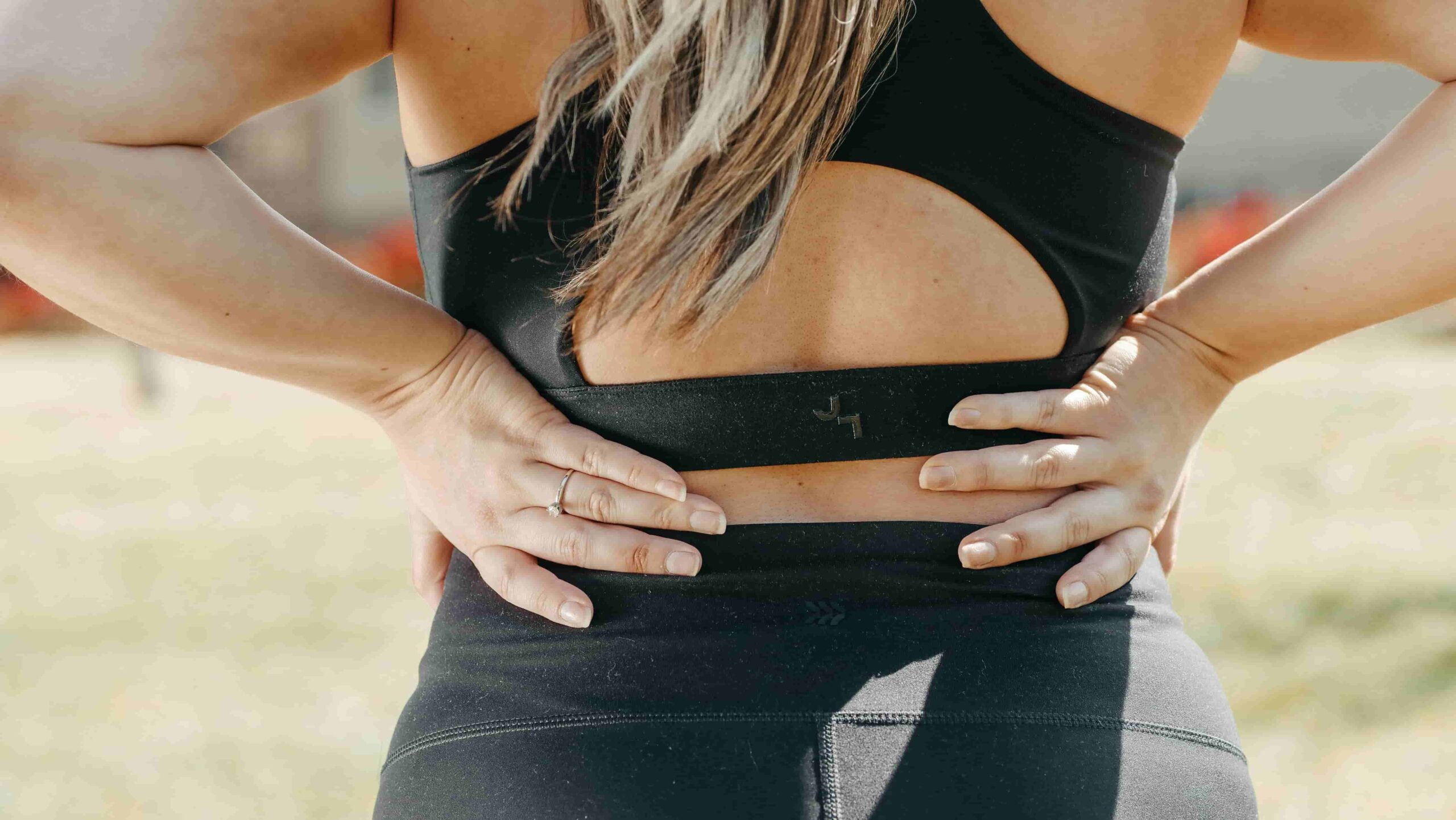 Person in athletic wear stands outdoors, facing away, with hands placed on their lower back as if experiencing discomfort—highlighting the need for massage therapy for chronic back pain in Coquitlam.