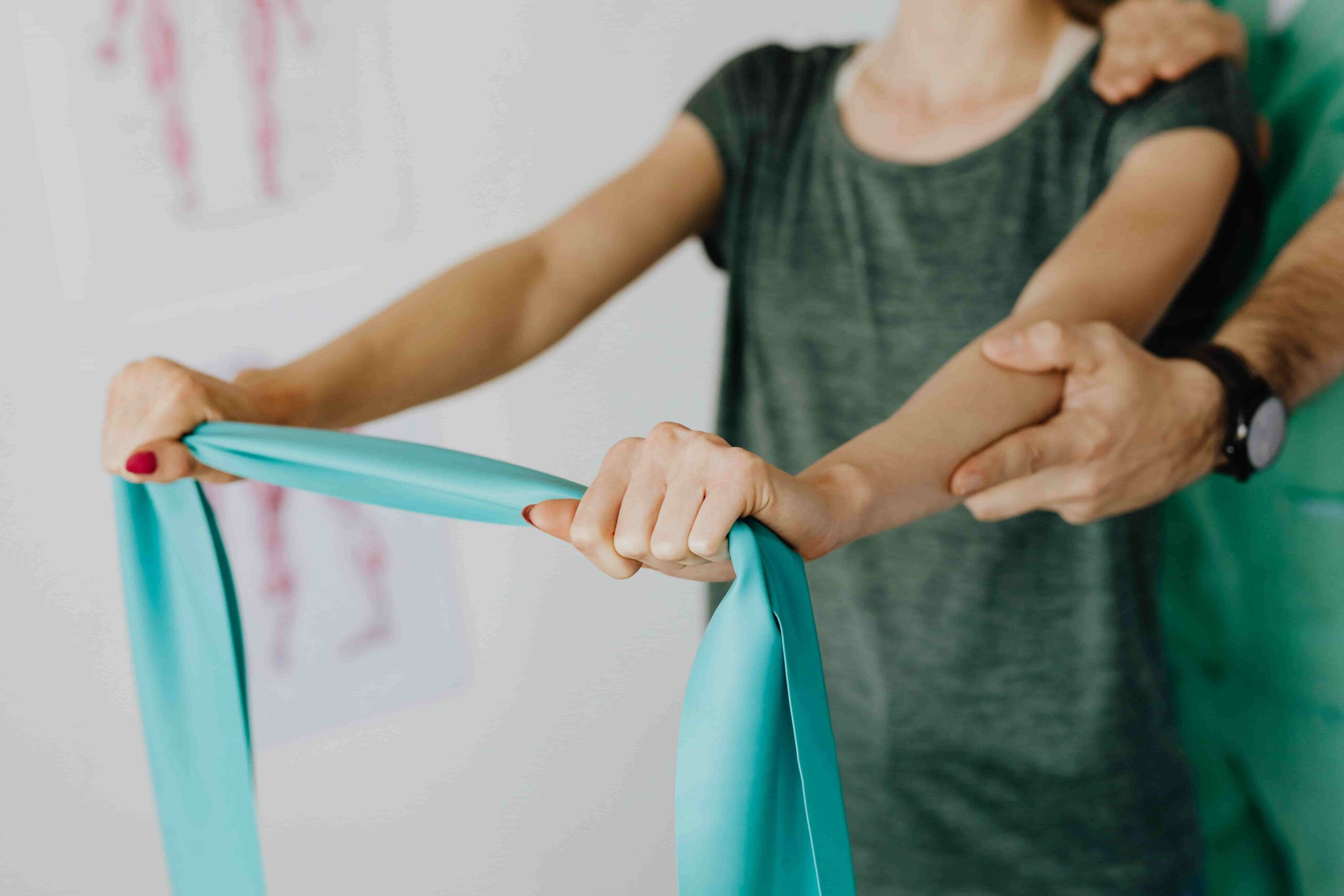 A person performs rehab exercises with a resistance band while another assists by supporting their arm.