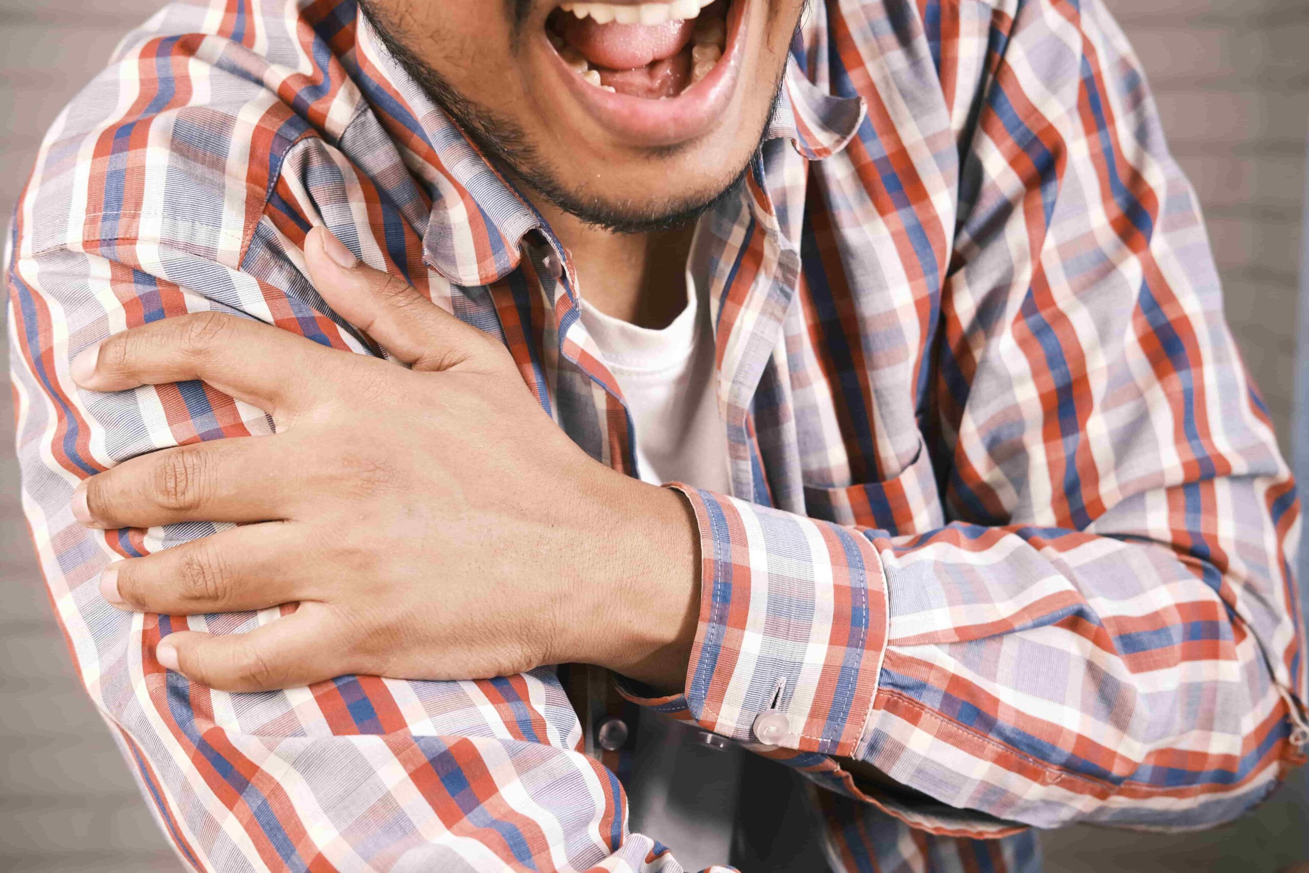 A person in a plaid shirt clutches their left shoulder and appears to be in pain, possibly seeking long-term chronic pain relief physiotherapy in Lonsdale, North Vancouver.