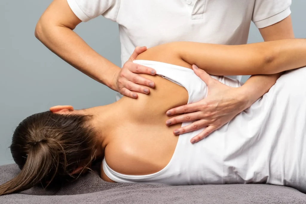 A person in a white shirt performs an osteopathy Coquitlam physical therapy adjustment on another person’s back and shoulder as they lie on their side.
