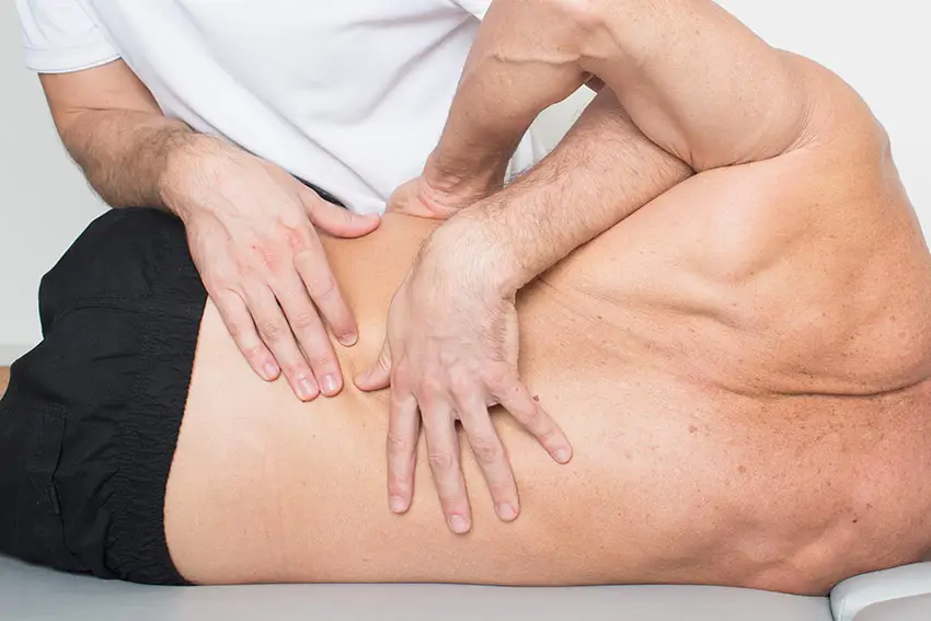 A person receives a chiropractic adjustment on their lower back while lying on their side on a treatment table, similar to techniques often used in osteopathy Coquitlam clinics.