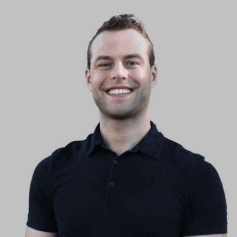 Smiling man with short brown hair wearing a black collared shirt, standing against a plain light gray background.