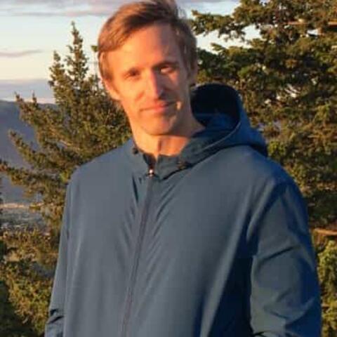 A person in a blue jacket stands outdoors with trees and hills in the background, under natural sunlight, enjoying some fresh air as part of their Active Rehab routine.