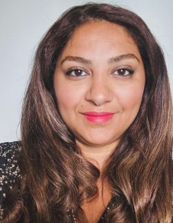 Maryam Haghshenas, a woman with long brown hair, wearing a black and white patterned top, smiles slightly while looking directly at the camera.